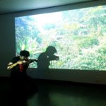 Andrea Lim pleying the violin at Titanik. Behind her is a video projection on the wall.