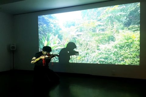Andrea Lim pleying the violin at Titanik. Behind her is a video projection on the wall.
